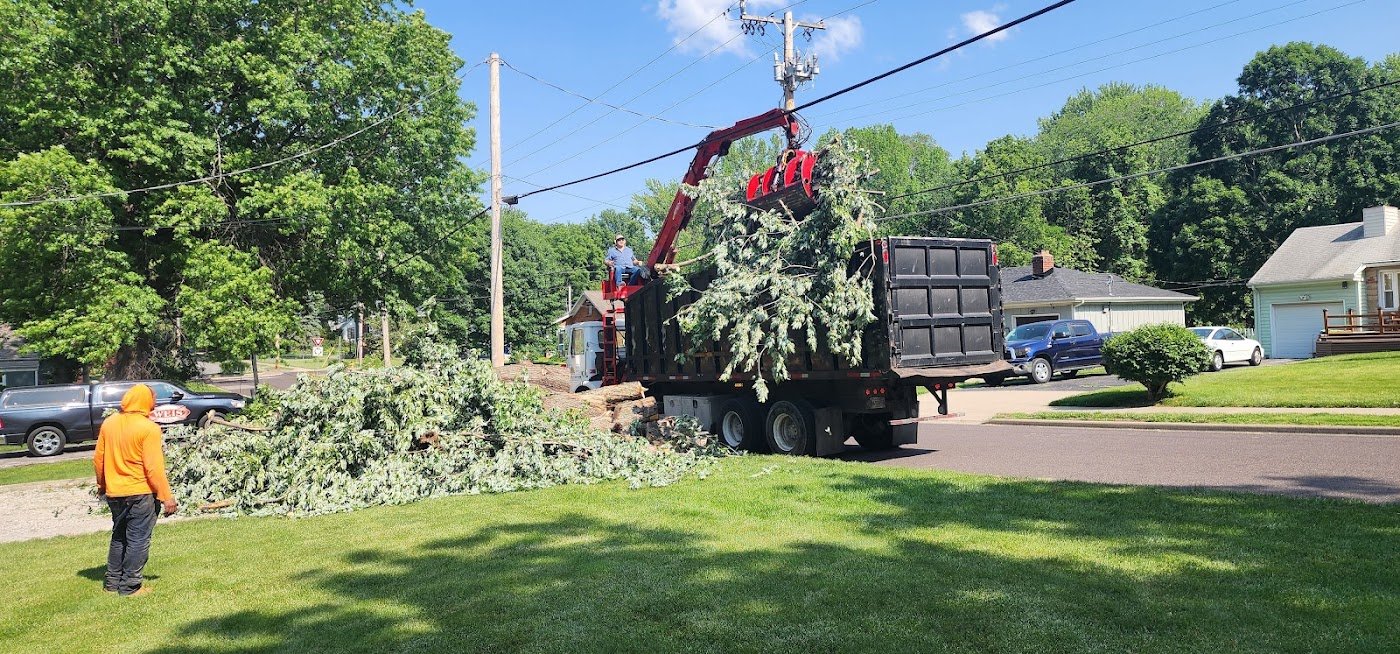 A grapple truck loading brush and limbs from a curbside removal.